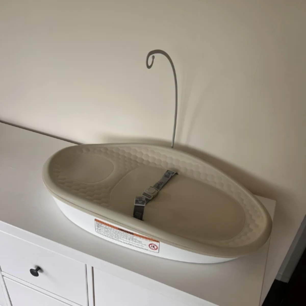 Bumbo change pad max insert with a taupe textured interior pad and a gray safety strap, shown on a white dresser against a beige wall.