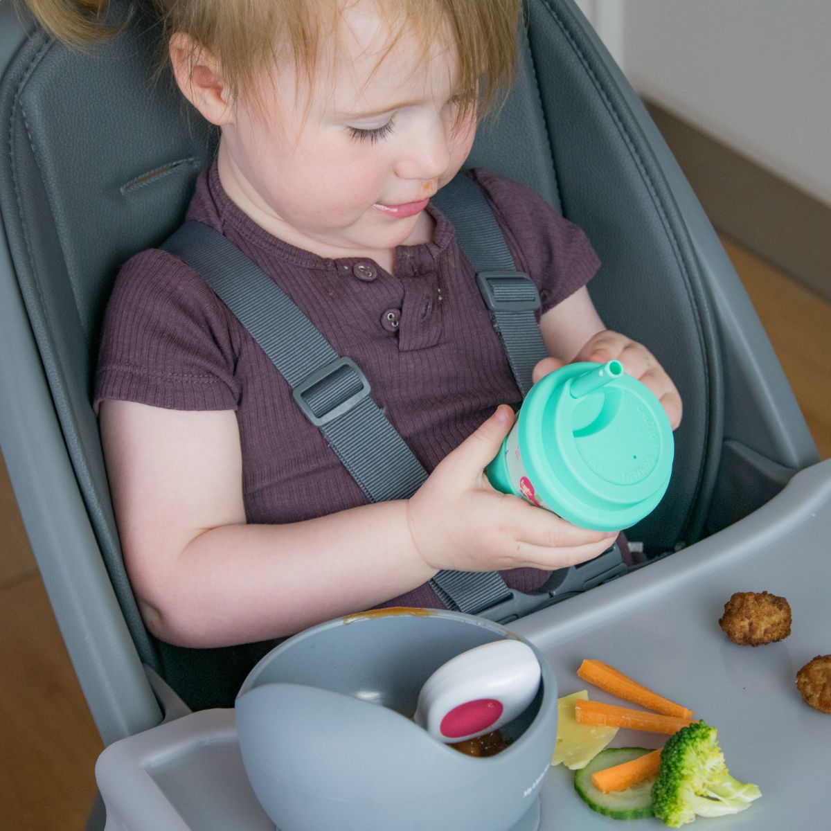 Toddler holding a cup in the Moose Harper highchair with food on the tray