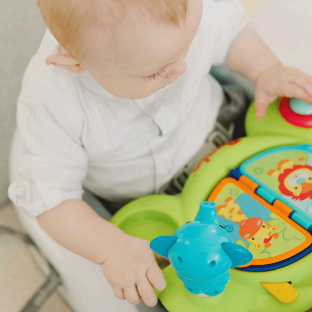 Overhead view of a baby exploring the colourful toys on the Bumbo Playtop Safari activity tray.
