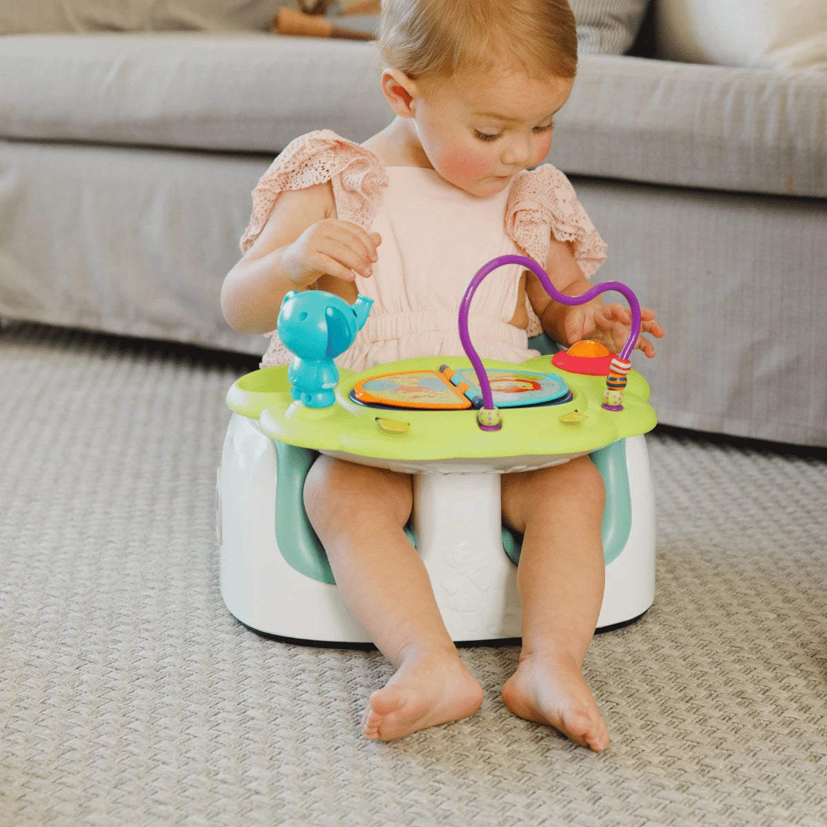 Baby seated on the floor in a Bumbo seat, playing with the Playtop Safari activity tray.