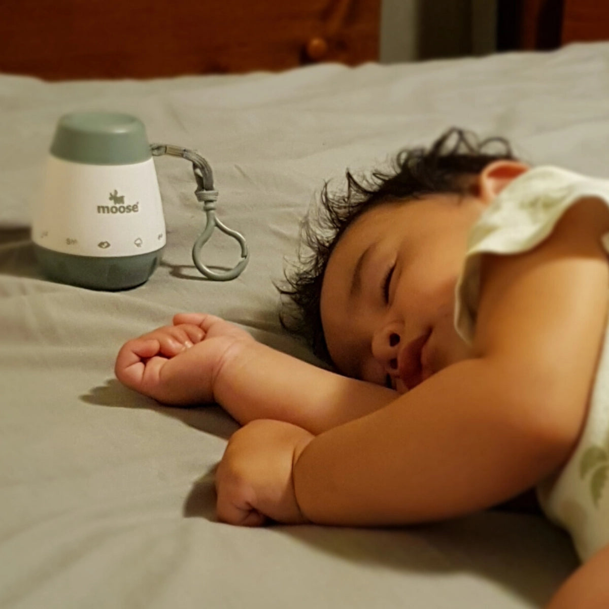 Sage green Calm-a White Noise Machine beside a sleeping baby on a bed