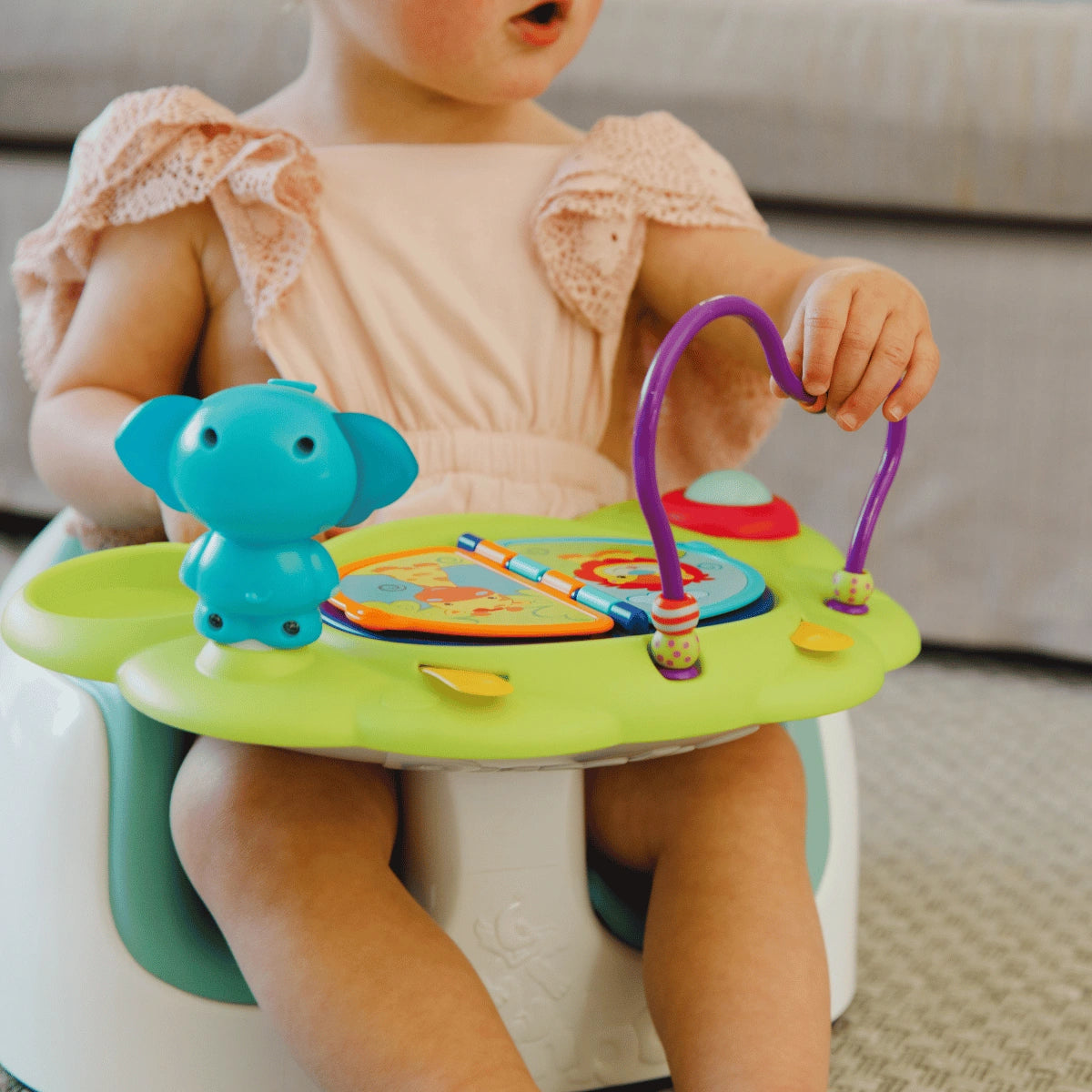 Close-up of a baby reaching for the toys on the lime green Bumbo Playtop Safari activity tray.