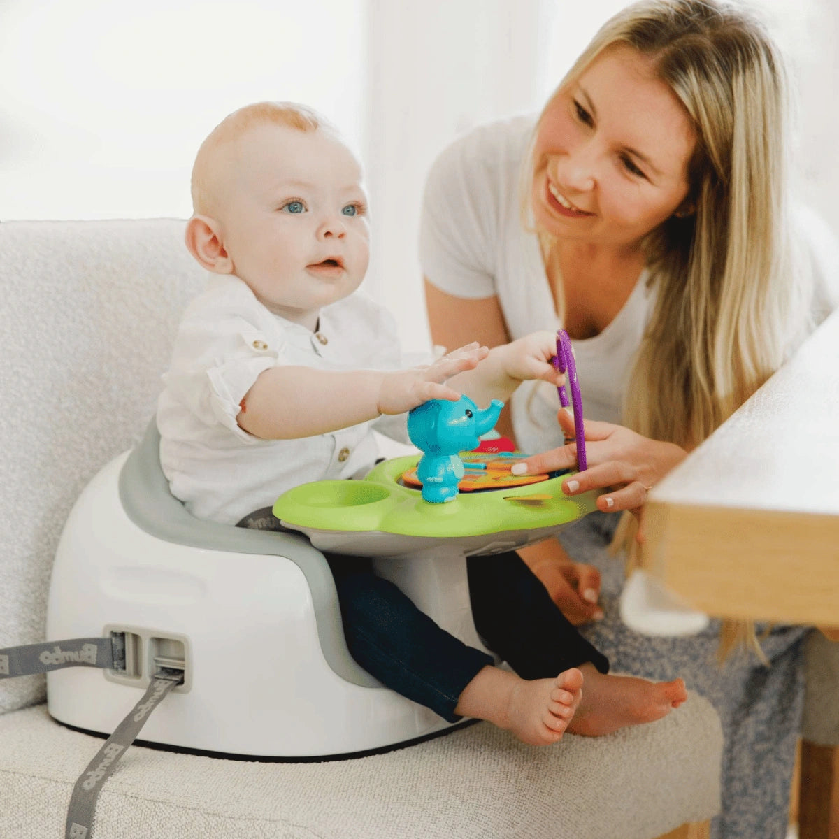 Baby playing with the Bumbo Playtop Safari activity tray while a woman sits beside the baby.