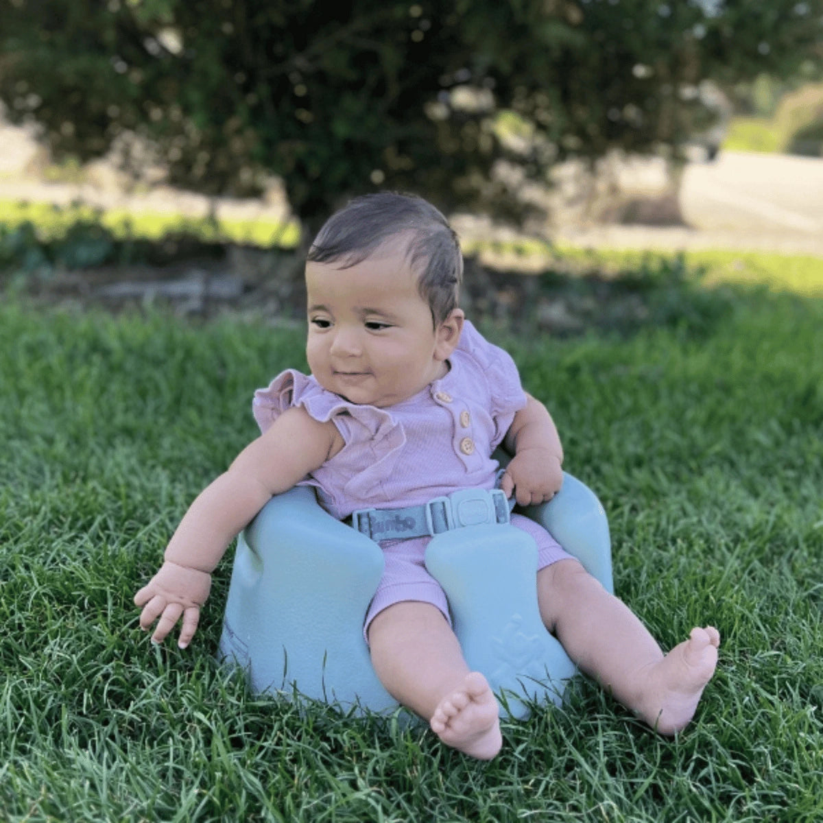 Bumbo Floor Seat Max in Saltbush with 3-point safety harness supporting a baby outdoors sitting on grassy lawn